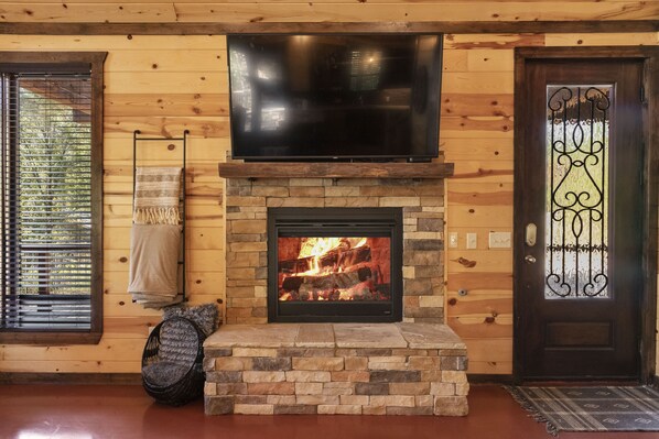 A fireplace with a TV above it, a door with a decorative glass panel, and a window with blinds.