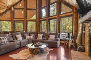 A spacious living room with a large sectional sofa, a glass coffee table, and a stone fireplace.