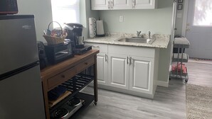 A kitchen with white cabinets, a refrigerator, a microwave, a coffee maker, and a stove. - Banana Beach Cottage (Lake Worth)