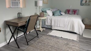 A bedroom with a bed, desk, chair, lamp, and artwork on the walls. - Banana Beach Cottage (Lake Worth)
