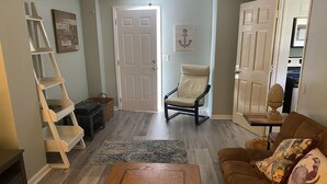 Ein Wohnzimmer mit Couchtisch aus Holz, braunem Sofa mit Dekokissen, weißem Sessel, einer Holzleiter und einem Teppich.