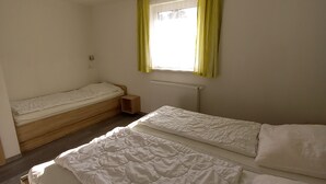 A room with two beds, a window with yellow curtains, a ceiling light, and a radiator.