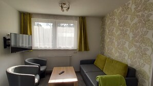 A modern living room with a sofa, two armchairs, a coffee table, and a TV mounted on the wall.