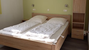 A single bed with a wooden frame and white bedding in a room with light green walls and a wooden wardrobe.