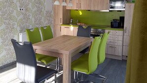 A modern kitchen with wooden cabinets, a built-in microwave, and a dining area with a wooden table and green chairs.