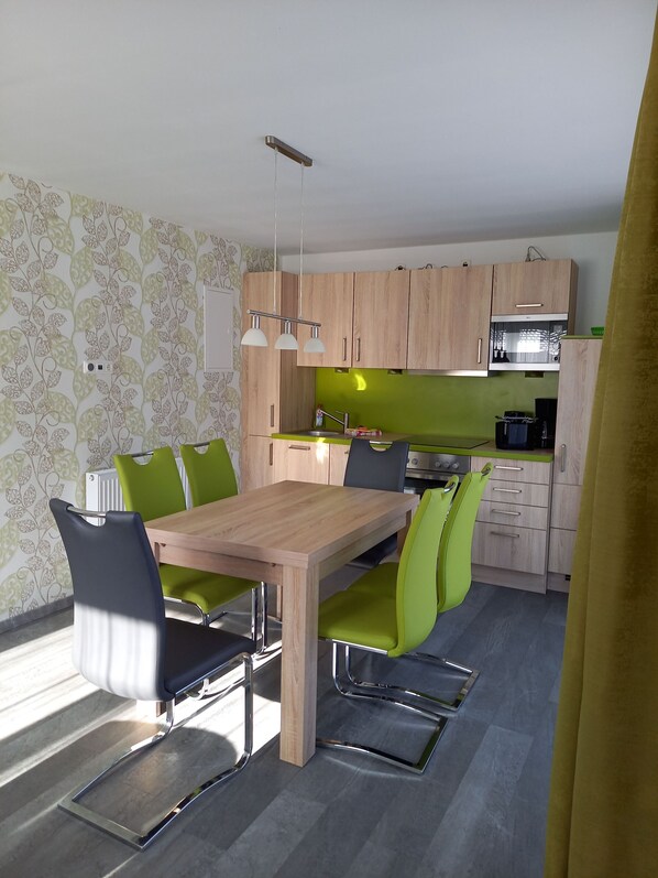 A modern kitchen with wooden cabinets, a built-in microwave, and a dining area with a wooden table and green chairs.