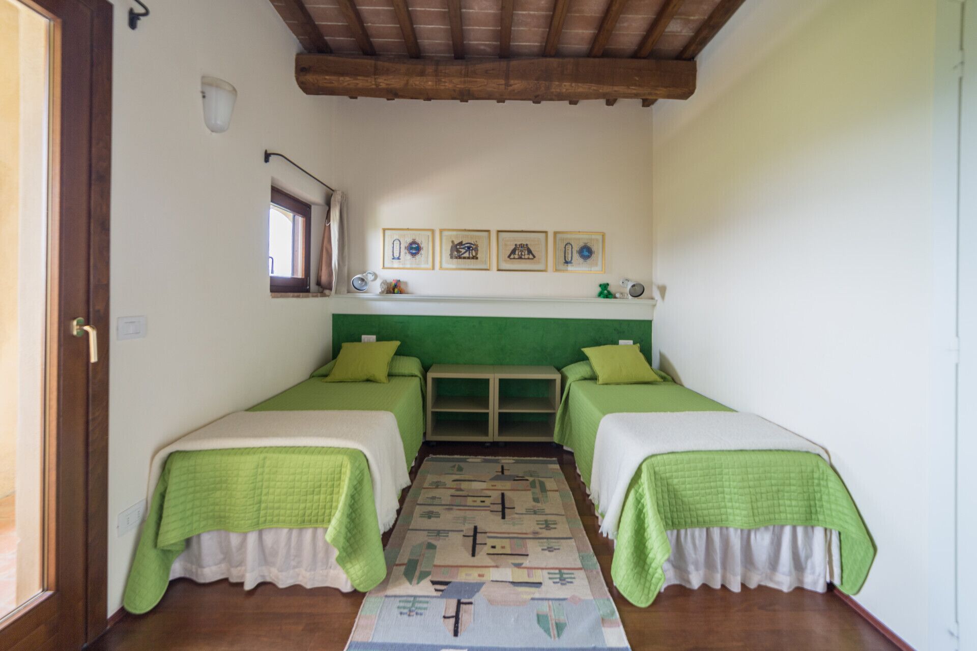 A room with two beds, a window, and a wall with framed pictures.