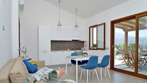 A modern kitchen with white cabinets, a dining area with blue chairs, and a large sliding glass door leading to an outdoor patio.