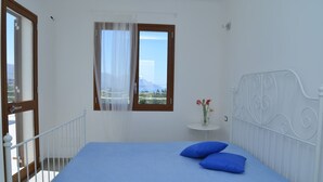 A bedroom with a bed, a window with a view, a small table with flowers, and a white railing.