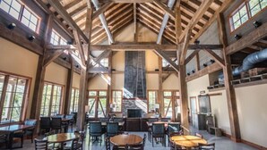 A spacious indoor area with high ceilings and wooden beams, featuring multiple tables and chairs arranged for dining or socializing. - Afton Escape-New Arcade, Winery Brewery EV-Charger (Afton)