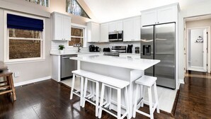 A modern kitchen with white cabinets, stainless steel appliances, and a large island with bar stools. - Afton Escape-New Arcade, Winery Brewery EV-Charger (Afton)