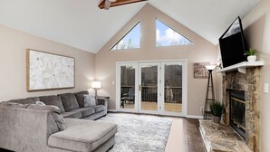 A living room with a grey sectional sofa, a fireplace, a TV mounted on the wall, and a large window allowing natural light. - Afton Escape-New Arcade, Winery Brewery EV-Charger (Afton)