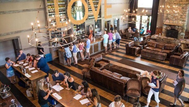A spacious bar area with multiple seating options, a prominent 'LOVE' sign, and a variety of bottles on shelves. - Afton Escape-New Arcade, Winery Brewery EV-Charger (Afton)