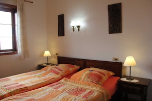 A double bed with a patterned bedspread, two bedside lamps, and a nightstand.