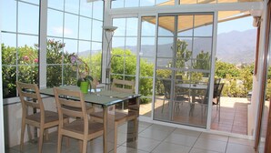 Une véranda dotée d’une table et de chaises en verre, entourée d’une terrasse offrant une vue sur les montagnes et la verdure.