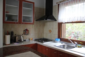 Una cocina con estufa a gas, un tostador y una ventana con vista a follaje.