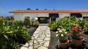 Una casa con techo de tejas, un sendero de piedra que lleva a la entrada y macetas con flores.