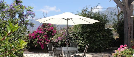 A patio with a round table and chairs, an umbrella, and surrounding greenery.