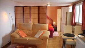 Een woonkamer met een bank, een salontafel, een keukenhoek met een koelkast, en een schuifdeur naar een andere kamer.