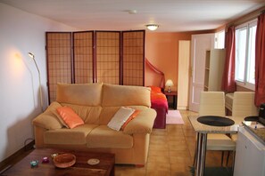 Ein Wohnzimmer mit einer Couch, einem Esstisch, einer Küchenzeile und einer Schiebetür zu einem weiteren Raum.