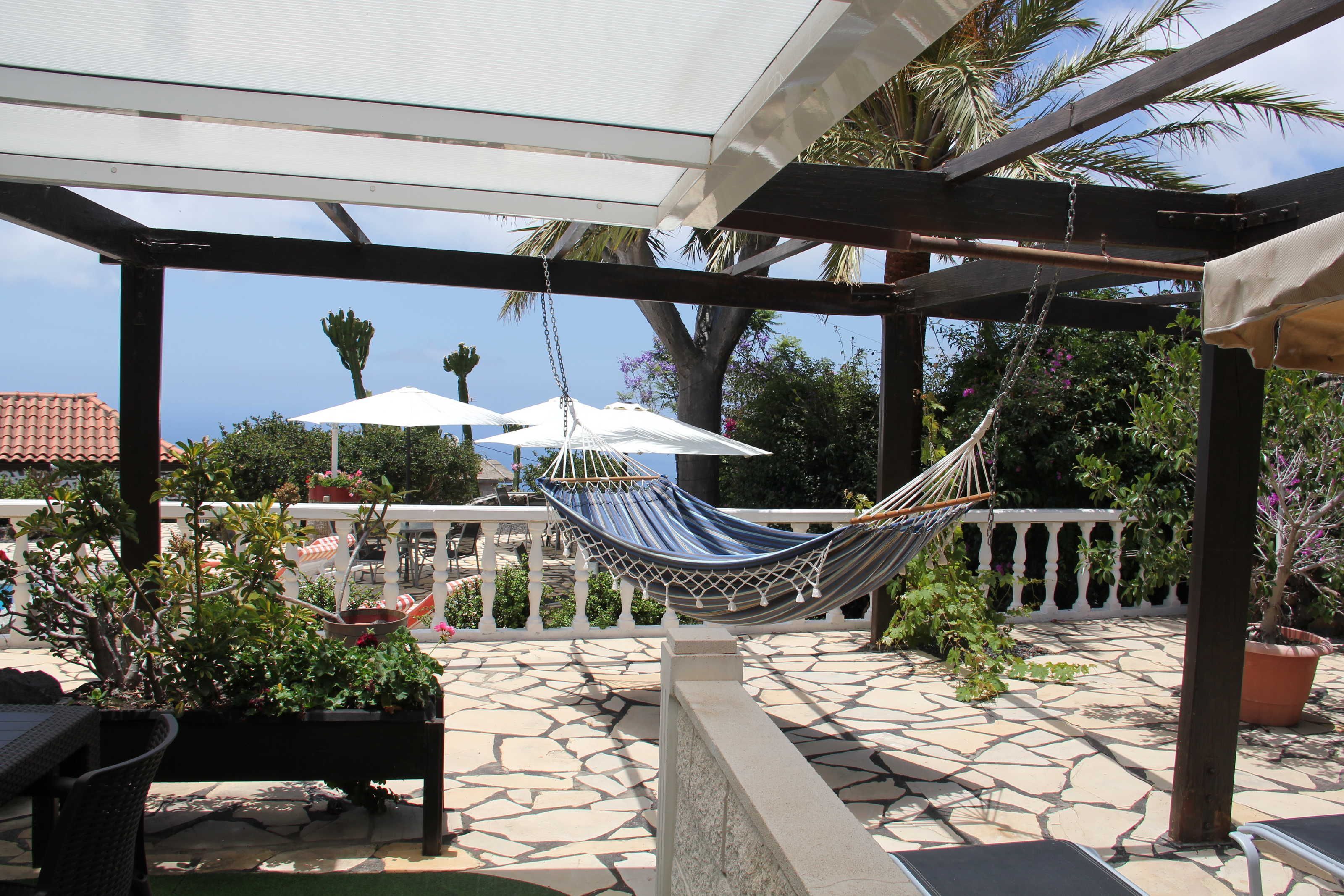 Un espace extérieur abrité, aménagé avec des sièges, un hamac, des plantes en pot et des parasols.