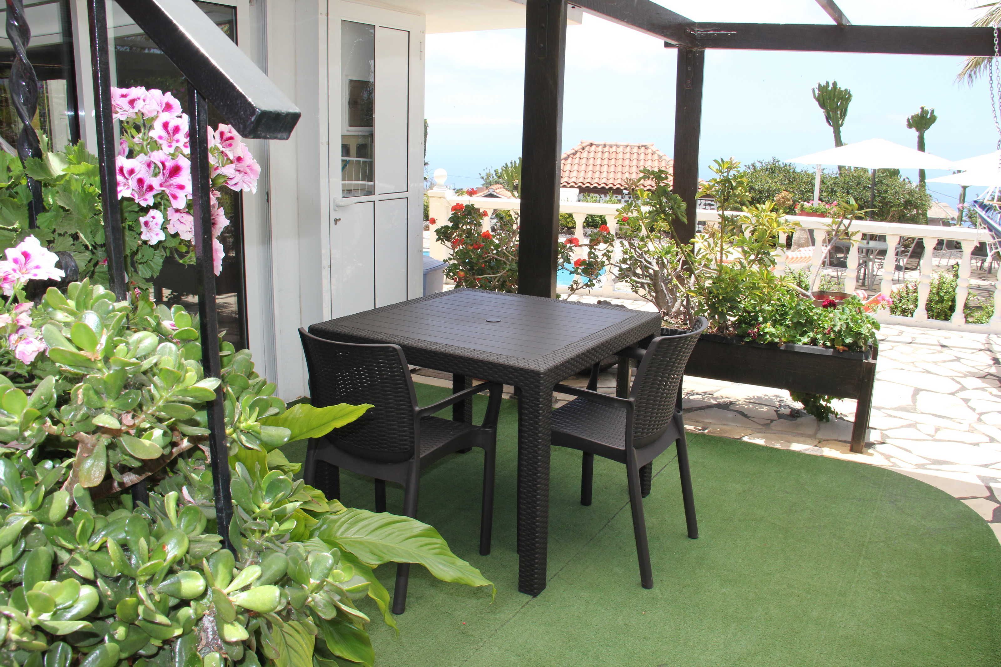 Eine Terrasse mit Tisch und Stühlen, umgeben von Grünpflanzen und Blick aufs Meer.