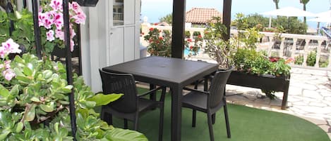 A patio with a table and chairs, surrounded by greenery and a view of the sea.