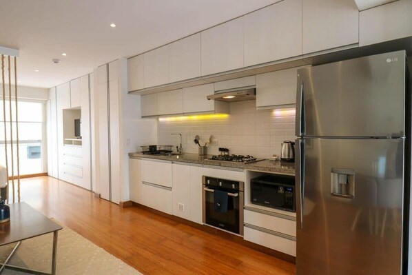 A modern kitchen with white cabinets, stainless steel appliances, and a wooden floor.