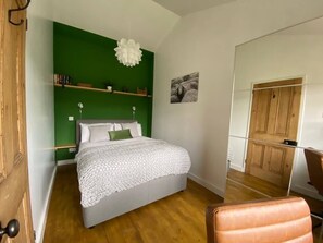 Un dormitorio con cama, pared de acento verde, lámpara de techo blanca, puerta de madera y sillón de cuero marrón.