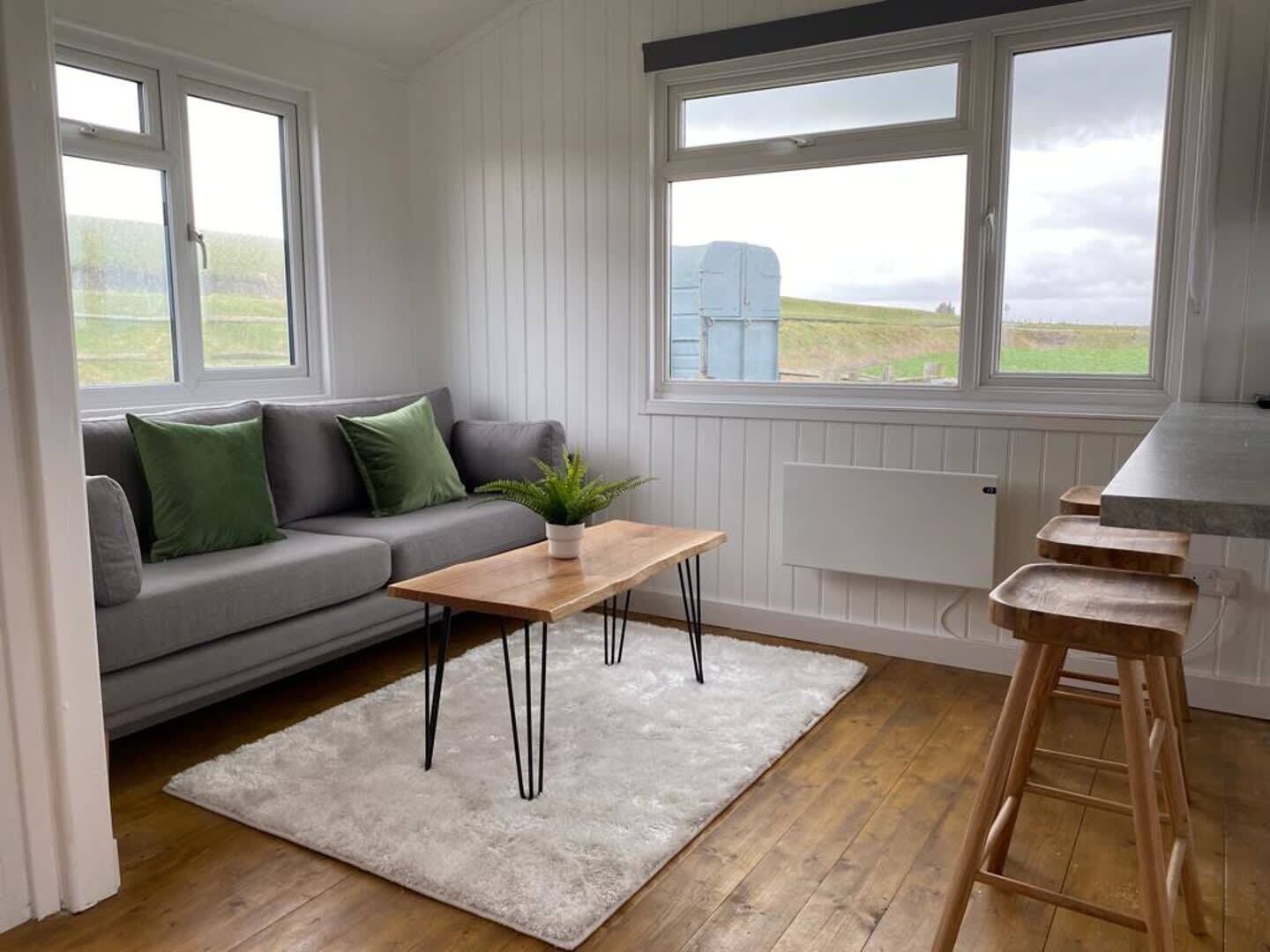 Een moderne woonkamer met een grijze bank, een houten salontafel en een wit vloerkleed.