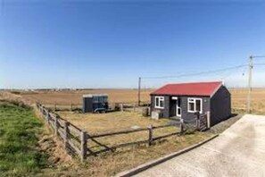 A small, single-story building with a red roof, a wooden fence, and a dirt road.