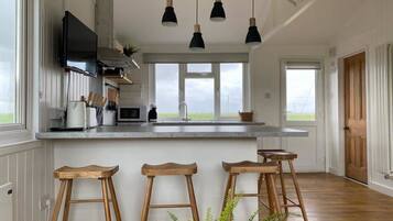 Een ruime keuken met een groot kookeiland, houten krukken, hanglampen en uitzicht op de omgeving.