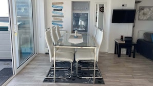 Un comedor con mesa y sillas de vidrio, vista al mar y un letrero que dice 'zarpazo'.