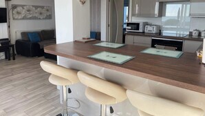 Una cocina moderna con armarios blancos, un microondas y un tostador. Hay una zona de comedor con una mesa de madera y taburetes de bar.
