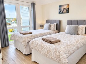 A hotel room with two beds, a large window with curtains, a painting on the wall, and a view of the outside.