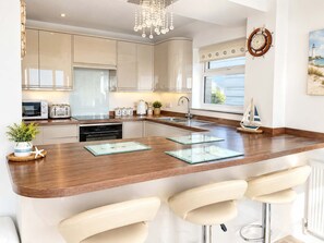 A modern kitchen with a central island, bar stools, a chandelier, and a sailboat decoration.