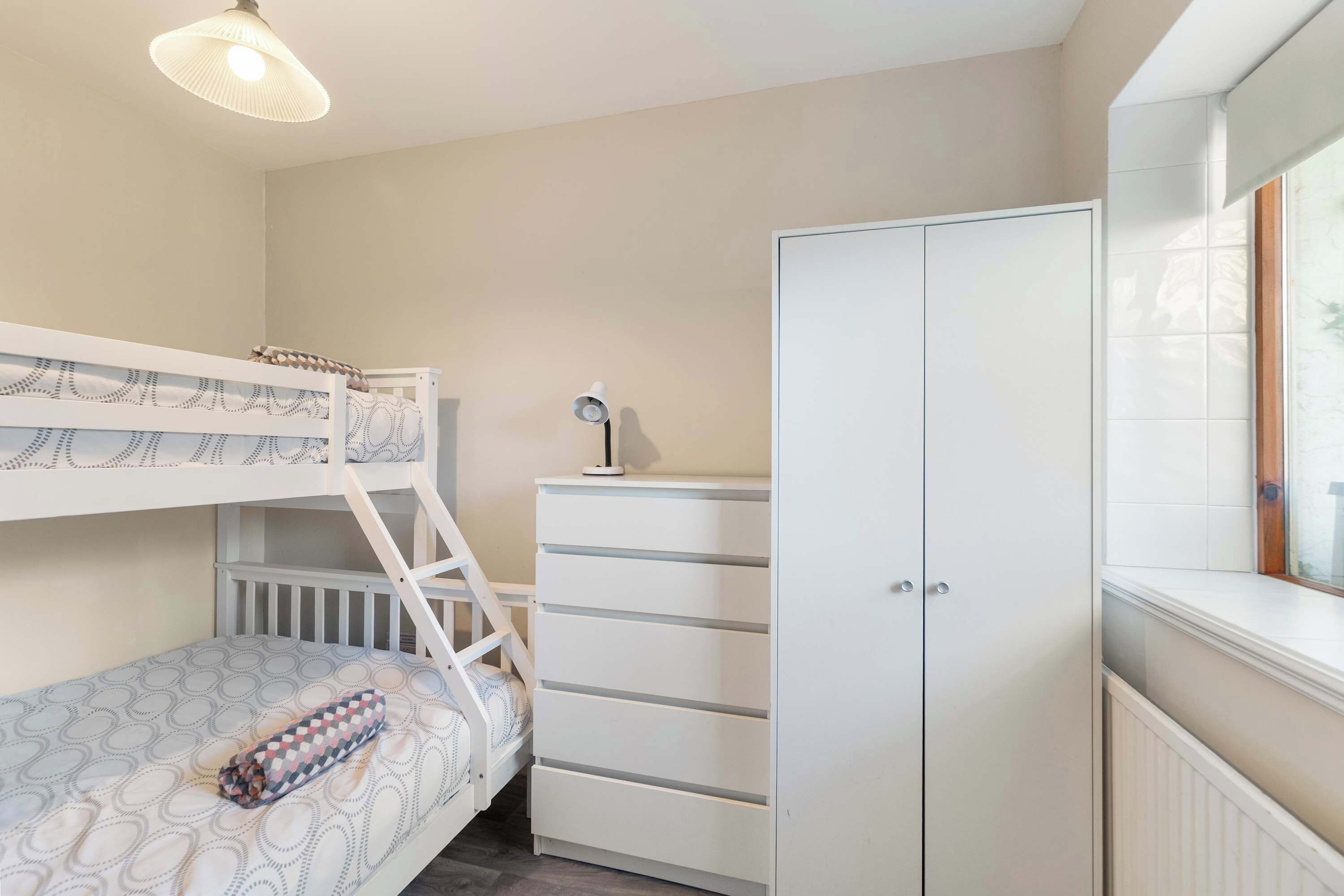 A bunk bed with a patterned mattress, a white dresser with drawers, and a lamp.