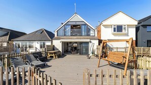 A coastal house with a deck, lounge chairs, and a swing. - Oceanfront Beach House - Family-Friendly (Pevensey)