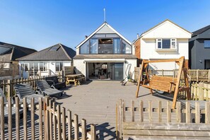 Une maison située sur la côte, dotée d’une terrasse, de chaises longues et d’une balançoire.