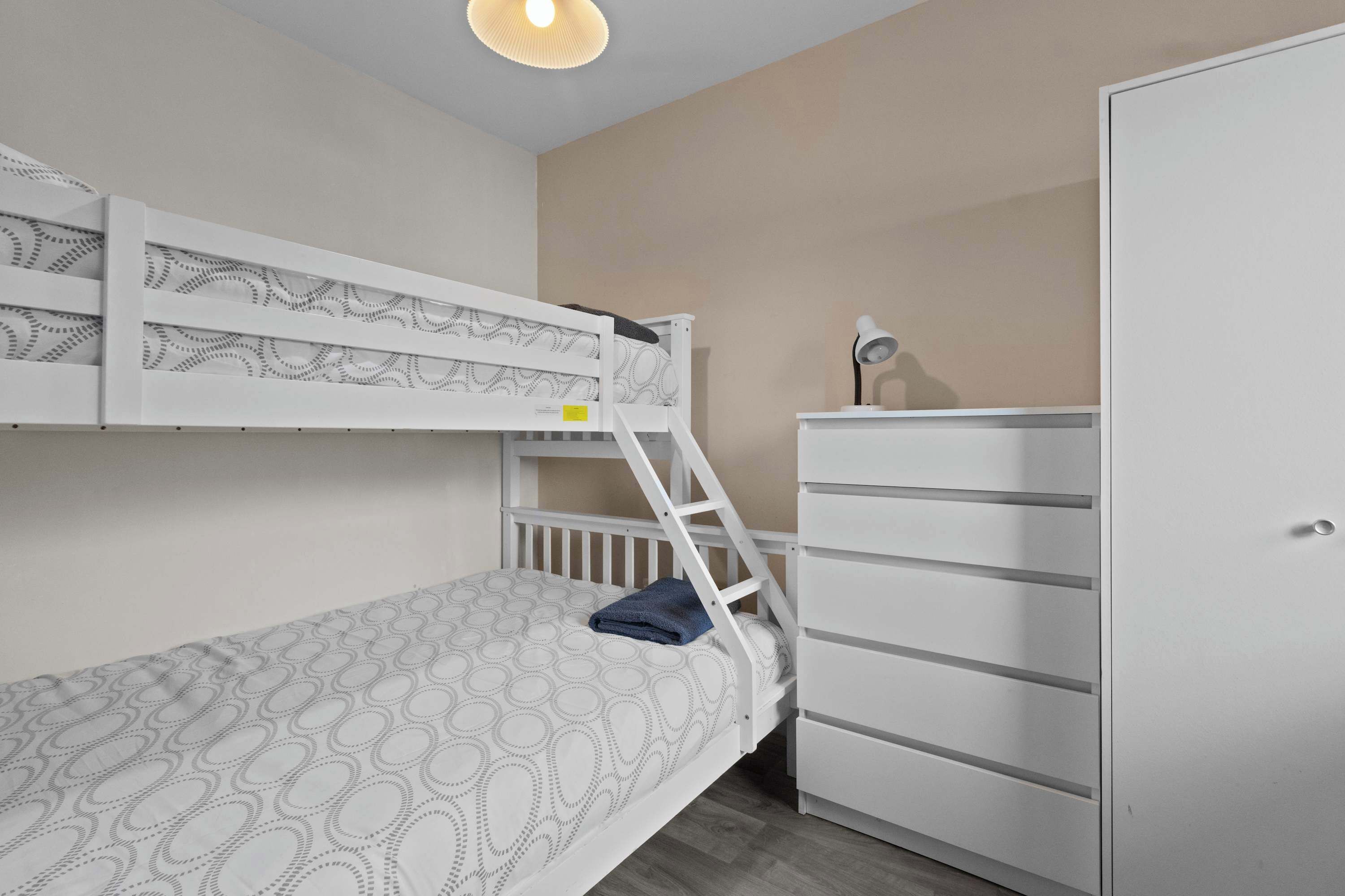 A bunk bed with a patterned mattress, a white dresser, and a desk lamp.