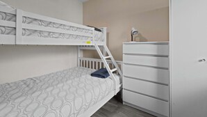 A bunk bed with a patterned mattress, a white dresser, and a desk lamp.