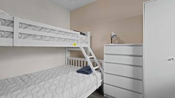 A bunk bed with a patterned mattress, a white dresser, and a desk lamp.