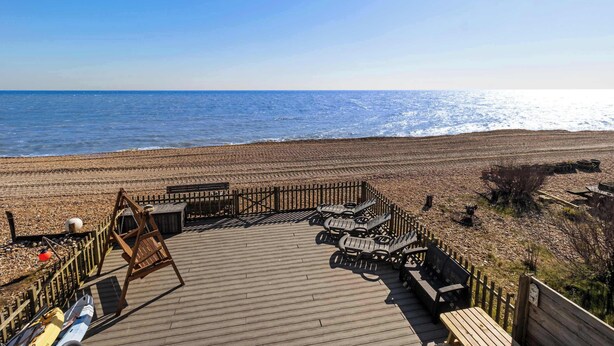 A wooden deck with lounge chairs overlooking a beach.