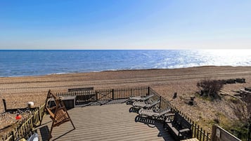 A wooden deck with lounge chairs overlooking a beach.