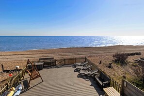 A wooden deck with lounge chairs overlooking a beach.