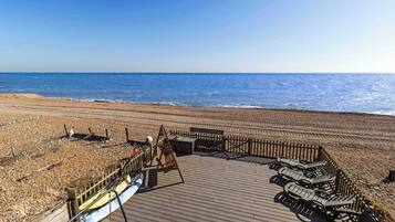 Une terrasse en bois avec des chaises longues et une clôture en bois donnant sur une plage.