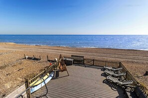 Una terraza de madera con sillones de descanso y valla de madera con vista a la playa.