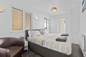 A modern bedroom with a large bed, bedside lamps, a chair, and a view through the window.