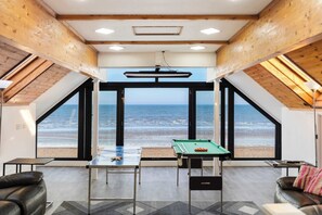 A room with a pool table, a sofa, and a view of the beach.