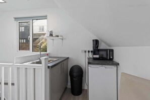 Una cocina compacta con un fregadero, un microondas y un pequeño basurero.